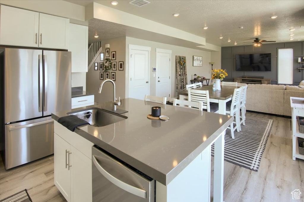 Kitchen with appliances with stainless steel finishes, a sink, a ceiling fan, light wood-style flooring, and white cabinets
