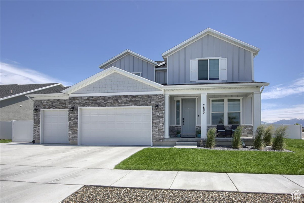 Craftsman-style house with board and batten siding, covered porch, an attached garage, concrete driveway, and stone siding