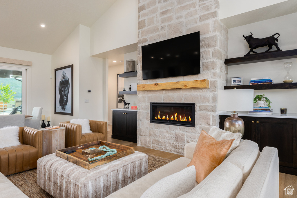 Living room with wood finished floors, a stone fireplace, and high vaulted ceiling