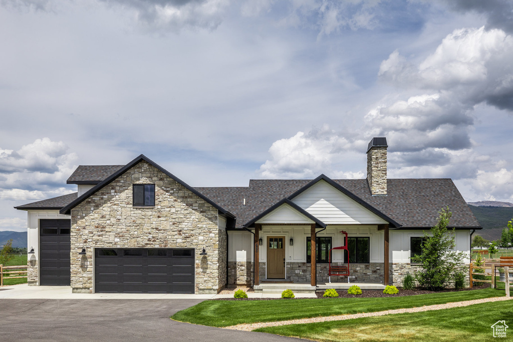 View of front of home featuring stone siding, driveway, a porch, a front yard, and a shingled roof