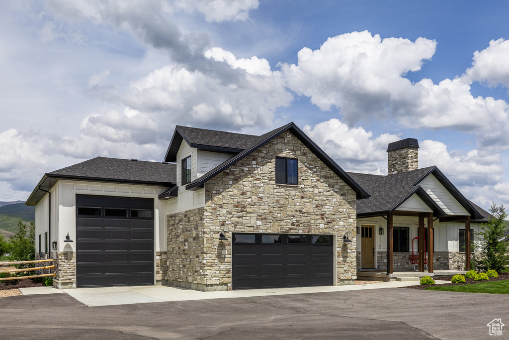 View of front facade with stone siding, asphalt driveway, a chimney, and a garage
