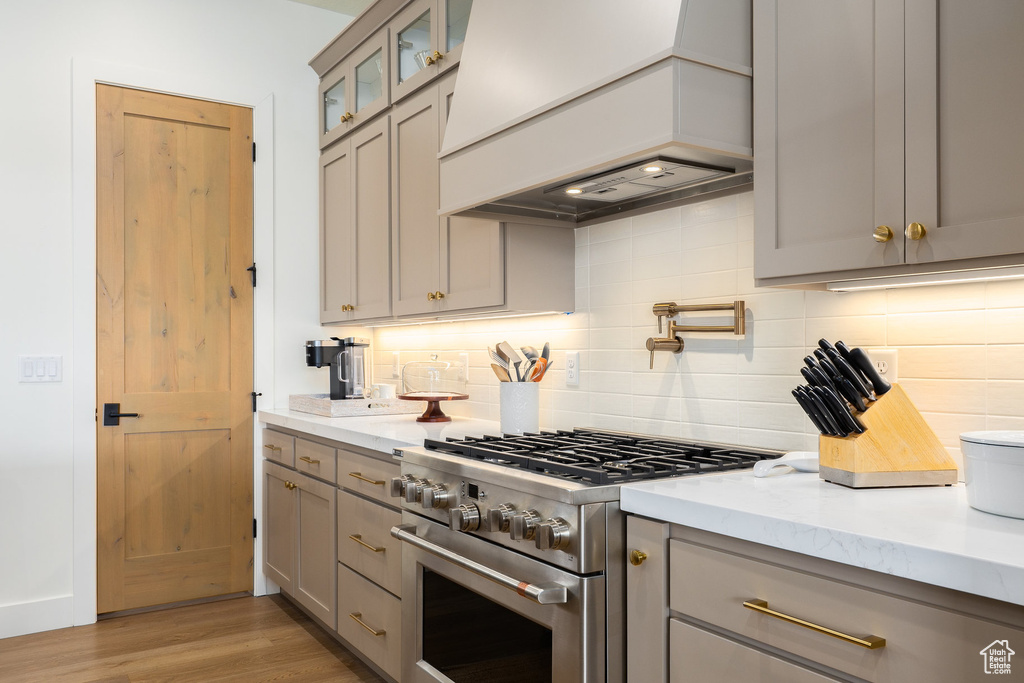 Kitchen with stainless steel stove, gray cabinets, custom exhaust hood, and backsplash