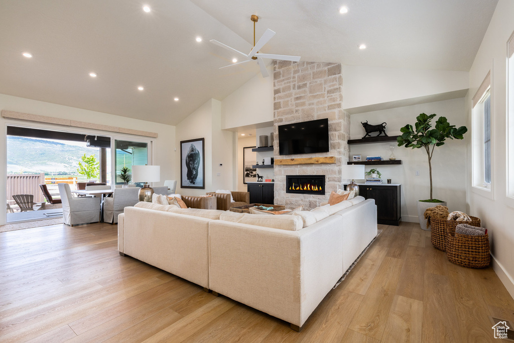 Living area with high vaulted ceiling, light wood-style flooring, a fireplace, a ceiling fan, and baseboards
