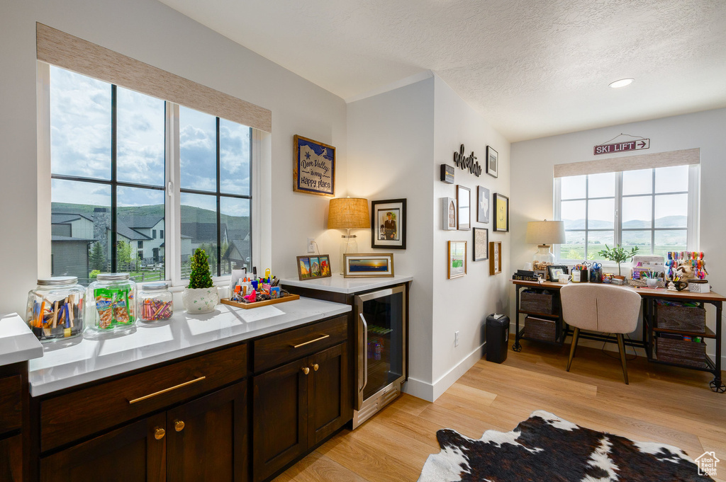 Kitchen featuring light wood-style flooring, beverage cooler, dark brown cabinetry, light countertops, and a textured ceiling