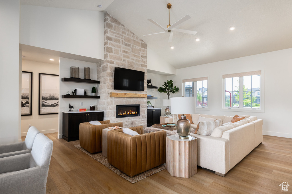 Living room with a ceiling fan, high vaulted ceiling, light wood-type flooring, a fireplace, and baseboards