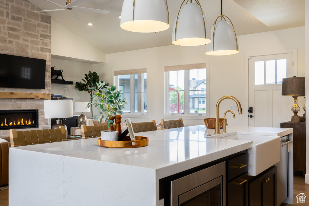 Kitchen with a center island with sink, a sink, open floor plan, a stone fireplace, and lofted ceiling