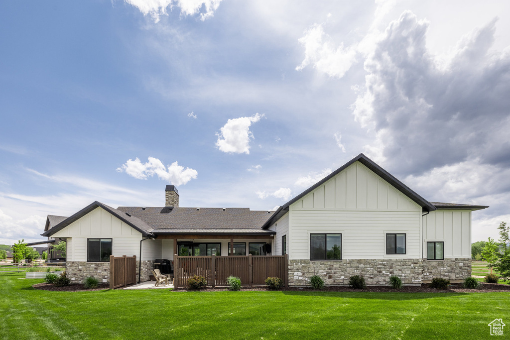 Rear view of property with board and batten siding, stone siding, and a yard