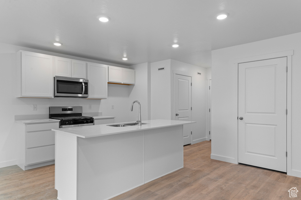 Kitchen with appliances with stainless steel finishes, a sink, white cabinets, an island with sink, and recessed lighting