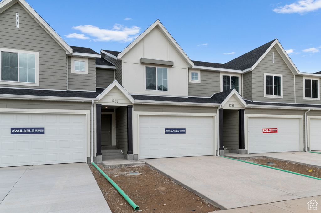 View of property featuring a garage, a shingled roof, and concrete driveway