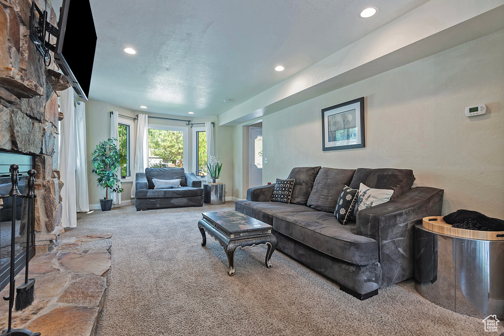 Carpeted living room with recessed lighting, a stone fireplace, and baseboards