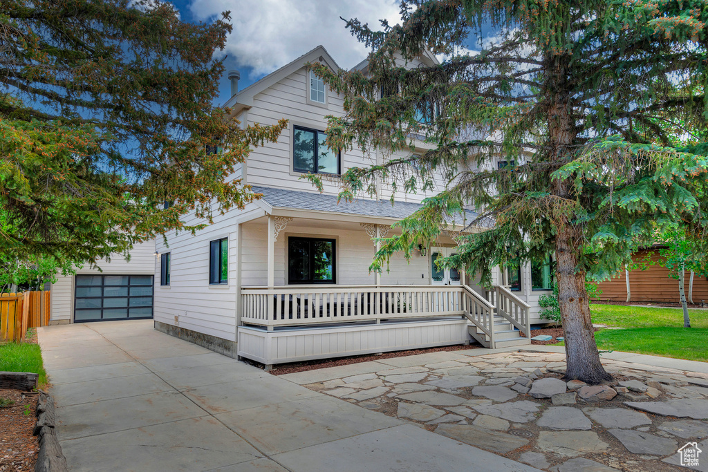 View of front of home featuring a porch, driveway, an outdoor structure, and roof with shingles