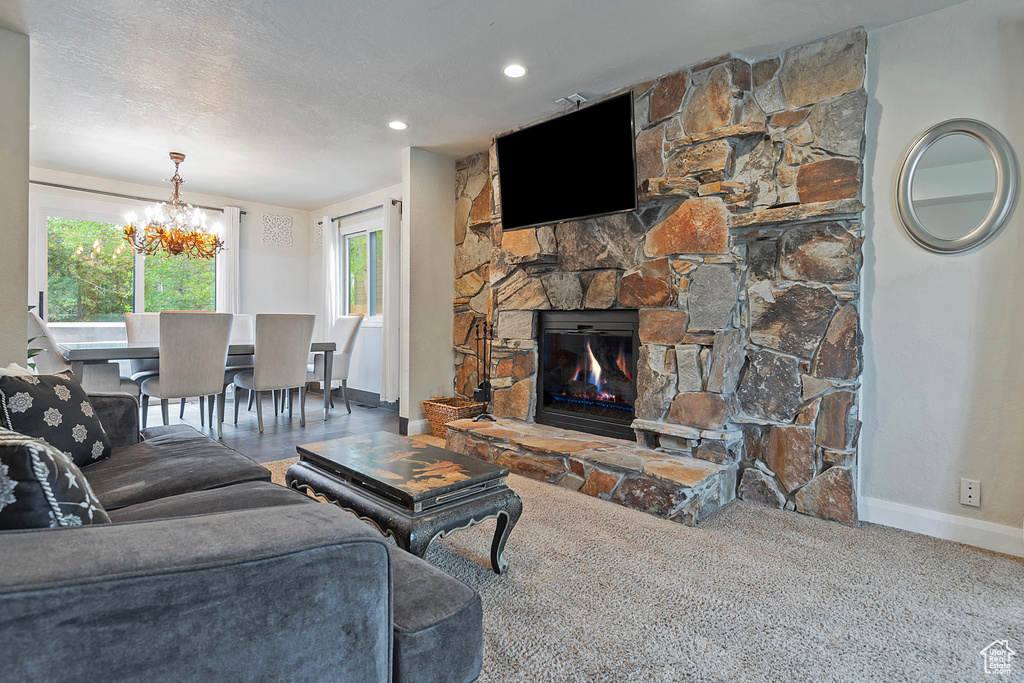 Carpeted living area featuring baseboards, a chandelier, and a stone fireplace