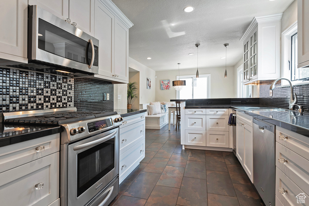 Kitchen with stainless steel appliances, dark countertops, backsplash, a peninsula, and a sink