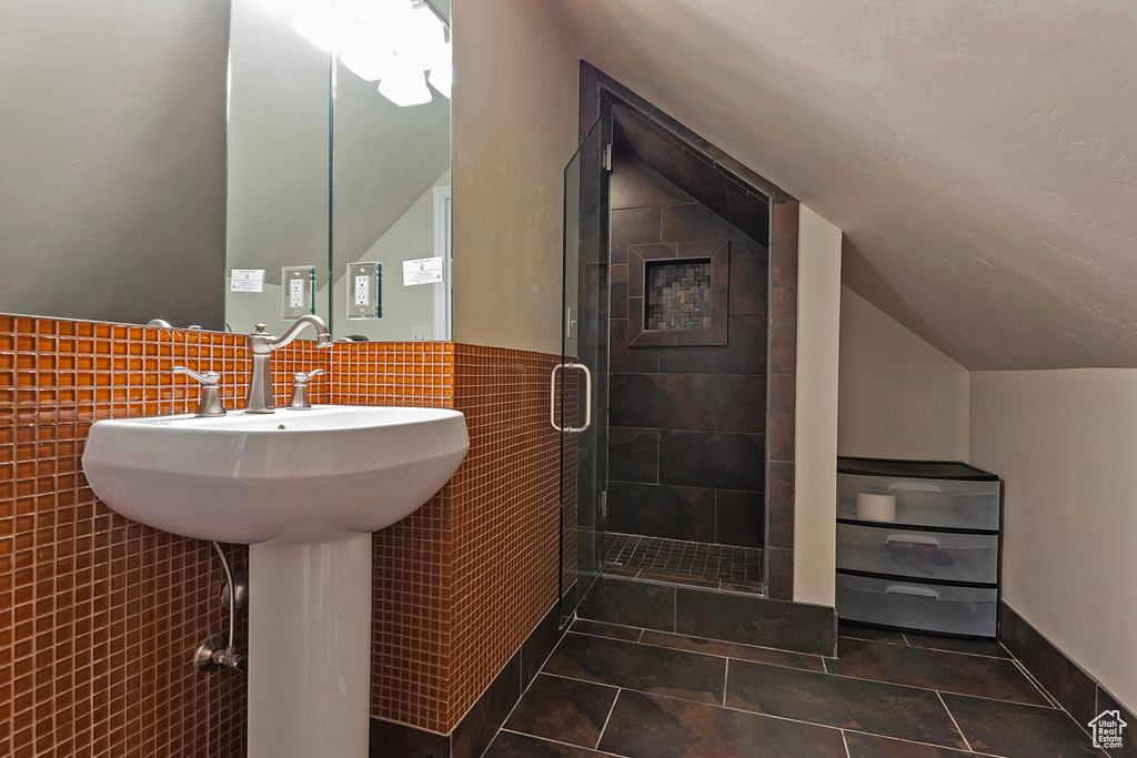 Bathroom featuring tile walls, vaulted ceiling, a shower stall, tile patterned floors, and wainscoting