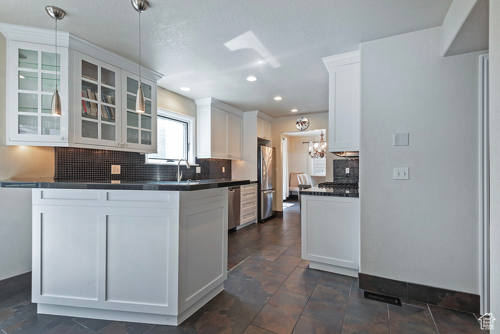 Kitchen with appliances with stainless steel finishes, dark countertops, glass insert cabinets, decorative backsplash, and white cabinets