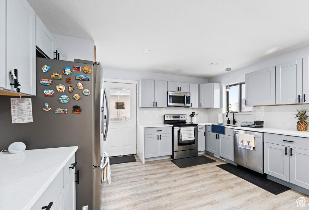Kitchen featuring appliances with stainless steel finishes, a sink, light wood-style floors, gray cabinets, and recessed lighting