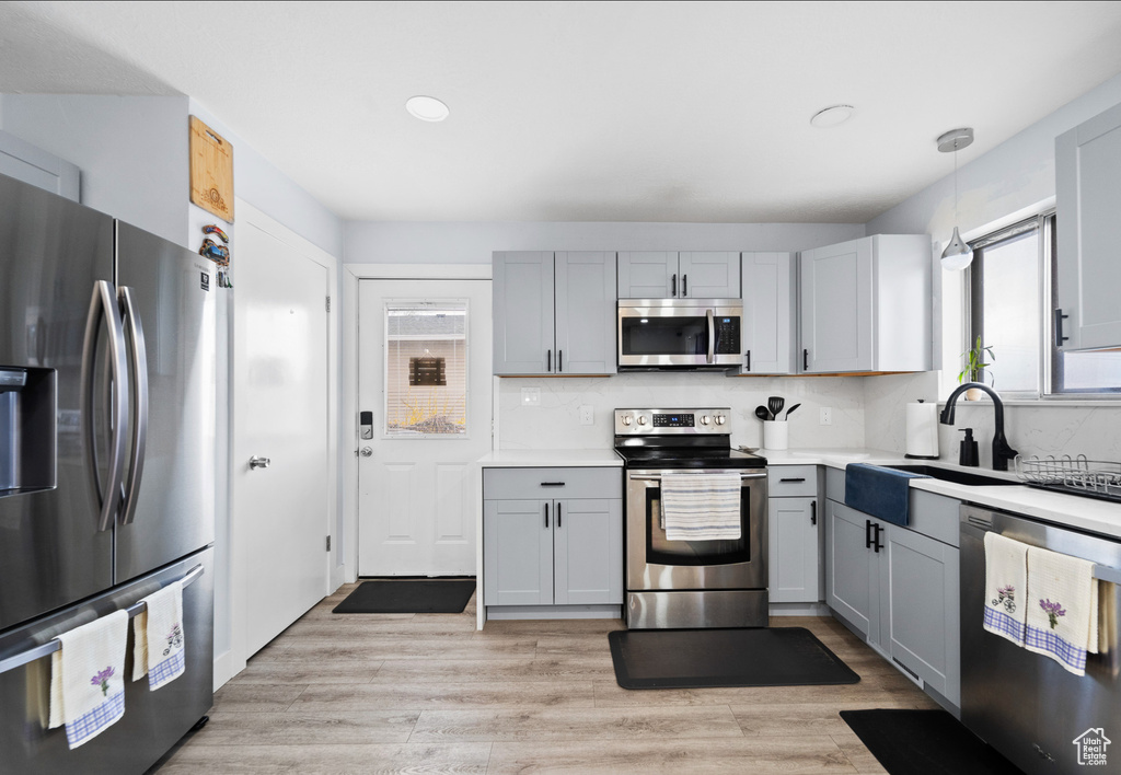 Kitchen featuring appliances with stainless steel finishes, gray cabinets, light countertops, tasteful backsplash, and a sink