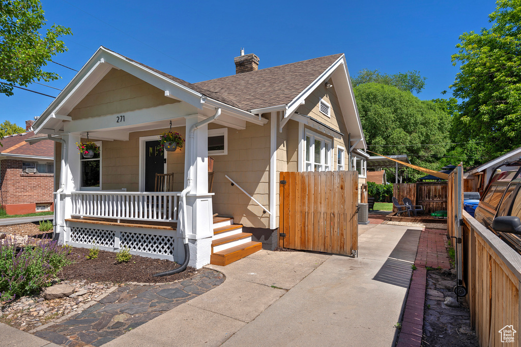 View of front of house with covered porch, a shingled roof, and a chimney