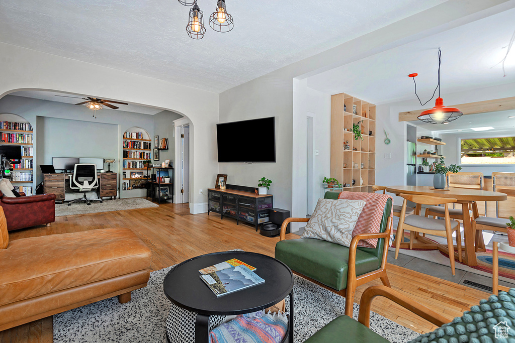 Living room with a desk, arched walkways, ceiling fan, wood finished floors, and built in shelves