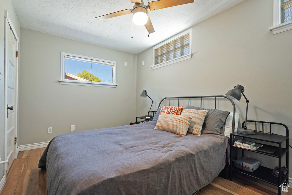 Bedroom with wood finished floors, baseboards, a textured ceiling, and ceiling fan