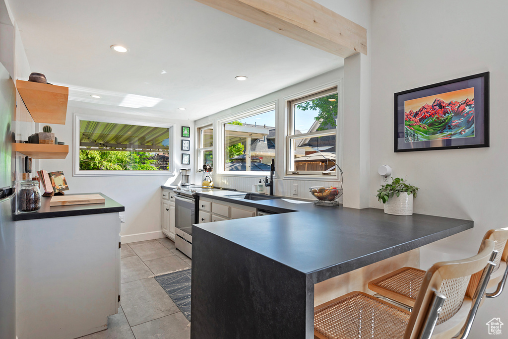 Kitchen with a sink, dark countertops, open shelves, a peninsula, and plenty of natural light