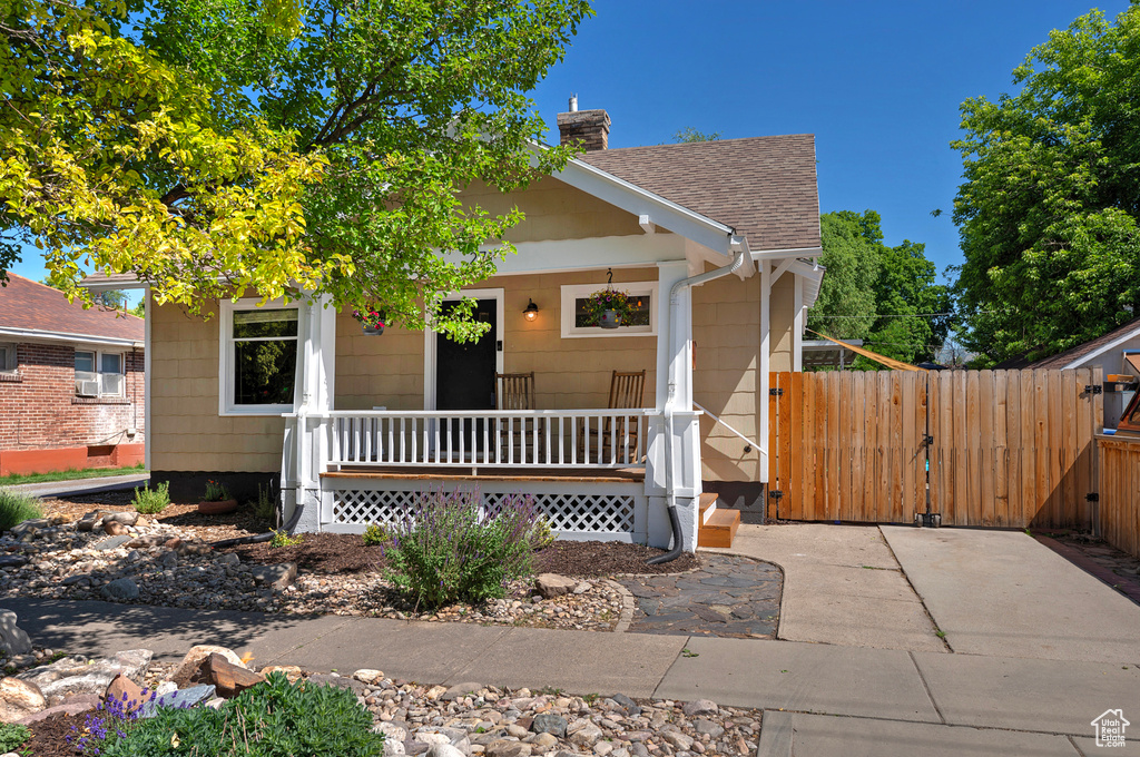 View of front of property with a porch, a gate, roof with shingles, and a chimney