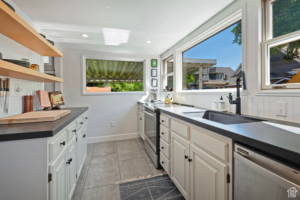 Kitchen with stainless steel appliances, open shelves, a sink, dark countertops, and white cabinetry