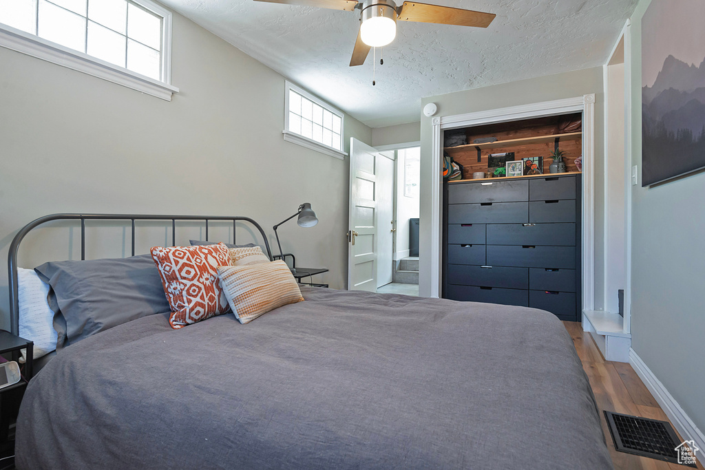 Bedroom with wood finished floors, a textured ceiling, ceiling fan, ensuite bath, and a closet