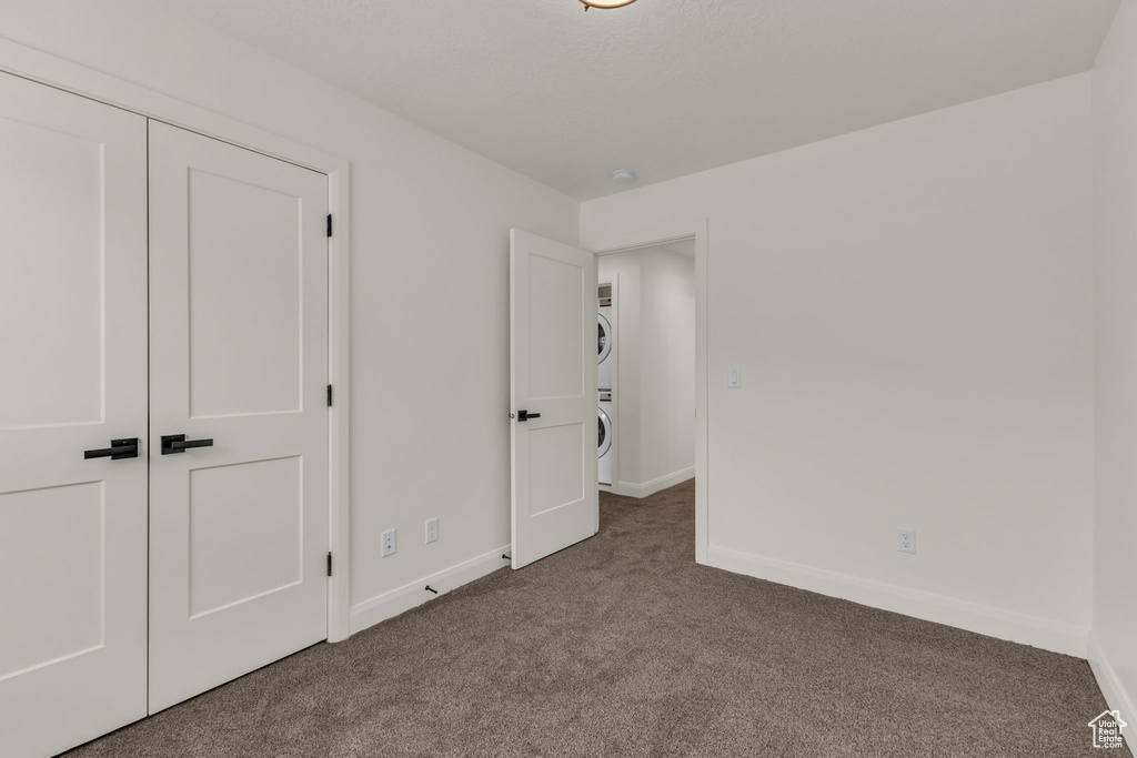 Unfurnished bedroom with stacked washing machine and dryer, carpet flooring, and baseboards