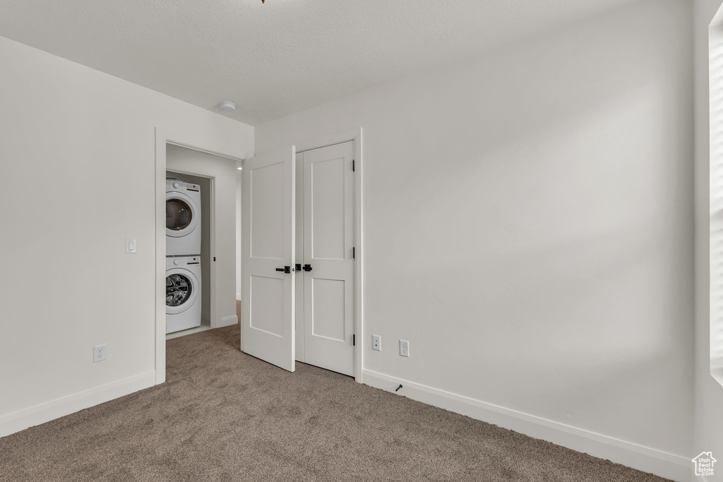 Empty room featuring estacked washer and dryer, carpet floors, and baseboards