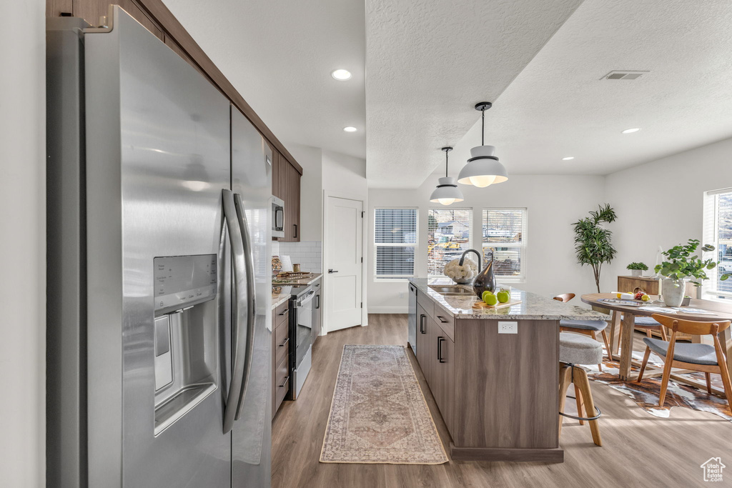 Kitchen with stainless steel appliances, light wood-style flooring, a kitchen island, a kitchen breakfast bar, and backsplash
