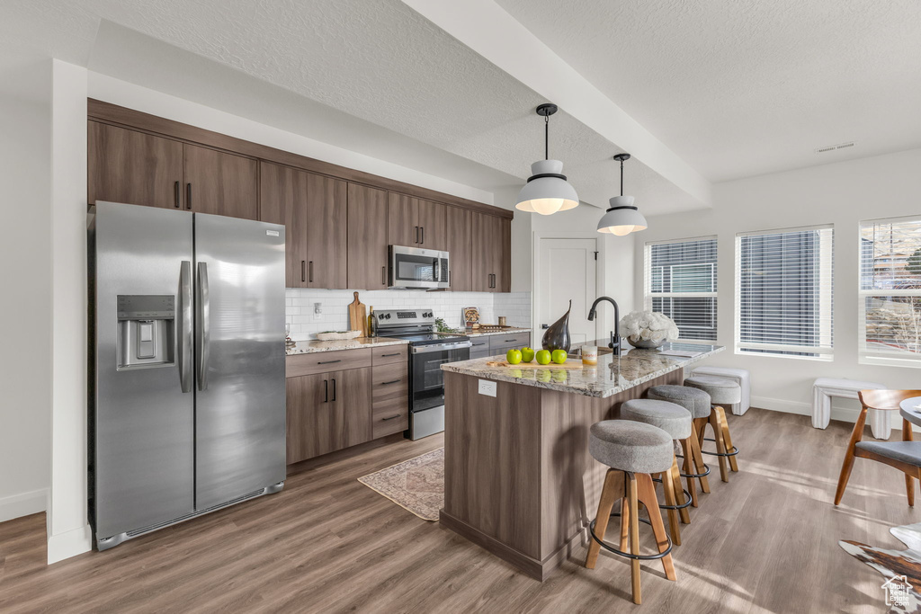 Kitchen with stainless steel appliances, a kitchen breakfast bar, wood finished floors, decorative backsplash, and a textured ceiling
