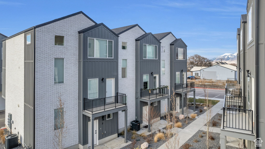 View of front of home featuring cooling unit, brick siding, board and batten siding, a balcony, and a mountain view
