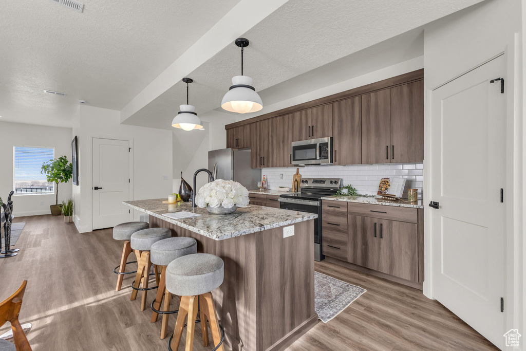 Kitchen with appliances with stainless steel finishes, a breakfast bar area, decorative backsplash, light wood-style floors, and a textured ceiling