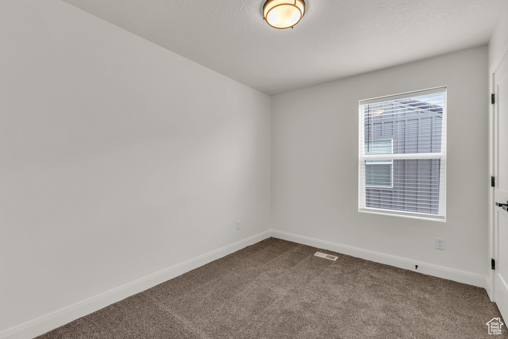 Spare room featuring dark colored carpet, baseboards, and a textured ceiling