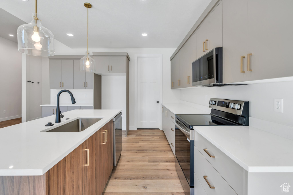 Kitchen featuring appliances with stainless steel finishes, light wood-type flooring, light countertops, pendant lighting, and recessed lighting