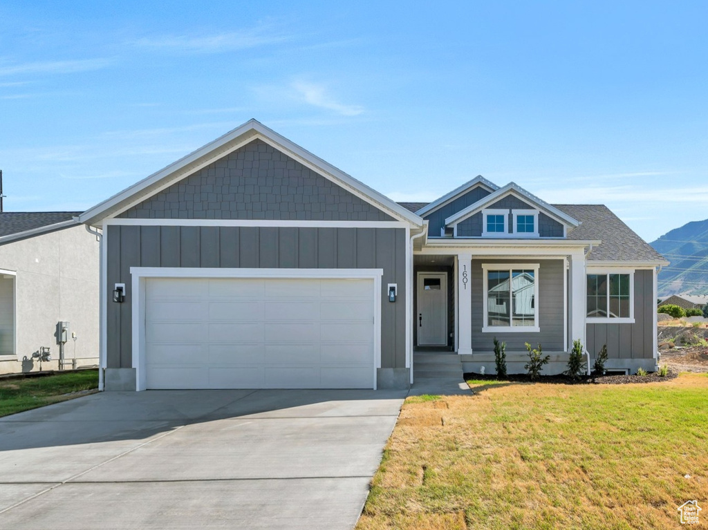 View of front of house with an attached garage, concrete driveway, a front yard, a mountain view, and board and batten siding