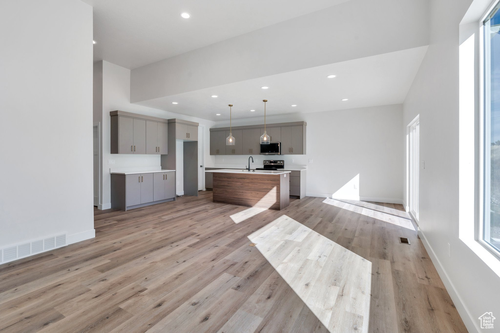 Kitchen featuring gray cabinets, stainless steel microwave, light wood-style flooring, a center island with sink, and recessed lighting