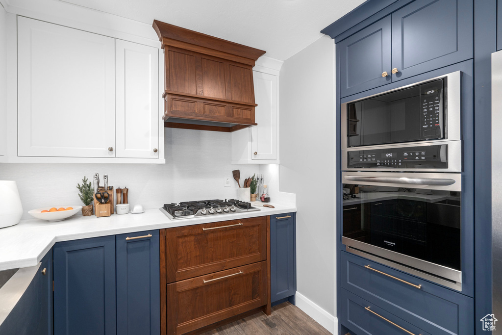 Kitchen featuring appliances with stainless steel finishes, blue cabinets, dark wood-type flooring, and white cabinetry