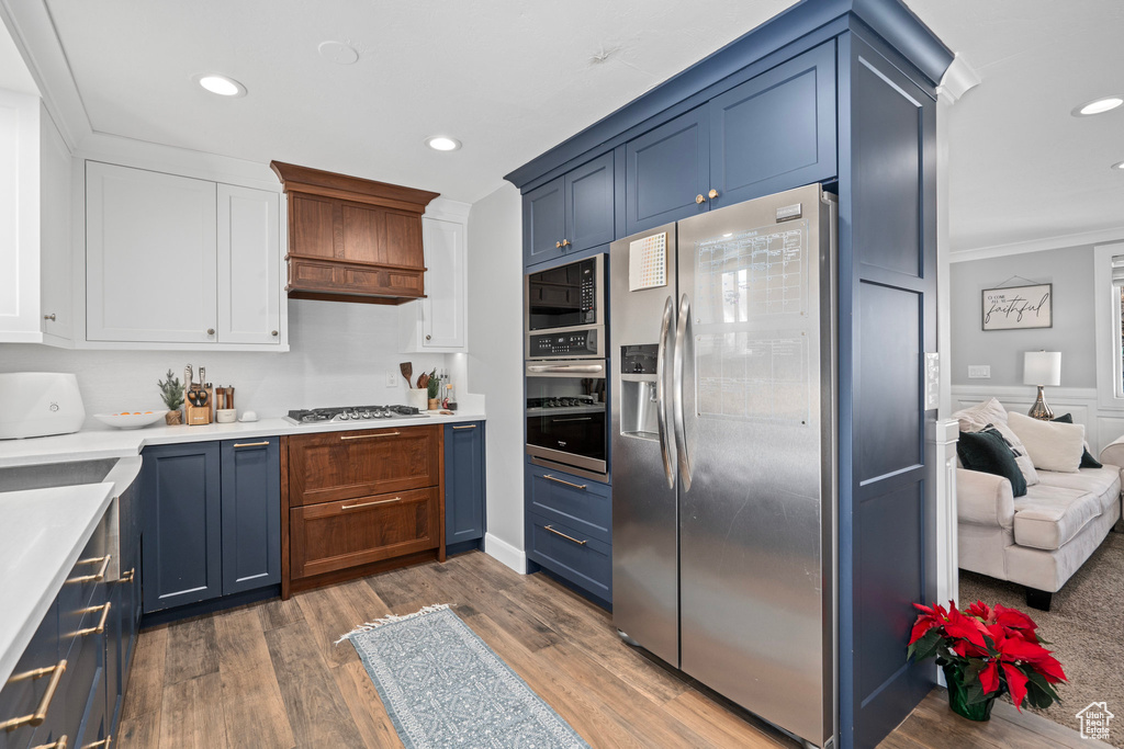 Kitchen with appliances with stainless steel finishes, ornamental molding, recessed lighting, light countertops, and white cabinetry