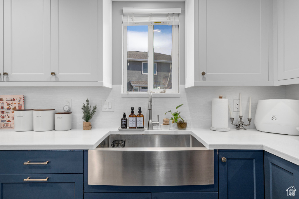 Kitchen featuring blue cabinets, a sink, white cabinets, backsplash, and light countertops