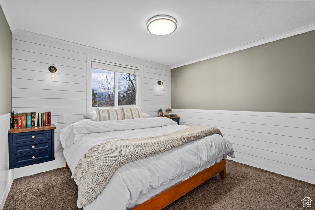 Bedroom featuring dark carpet, wood walls, and ornamental molding