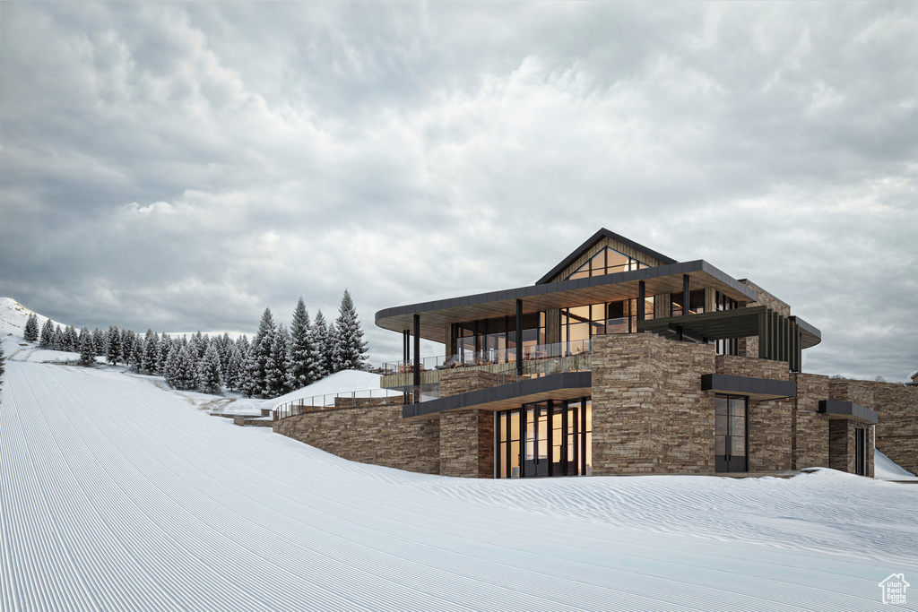 Snow covered house featuring stone siding and a balcony