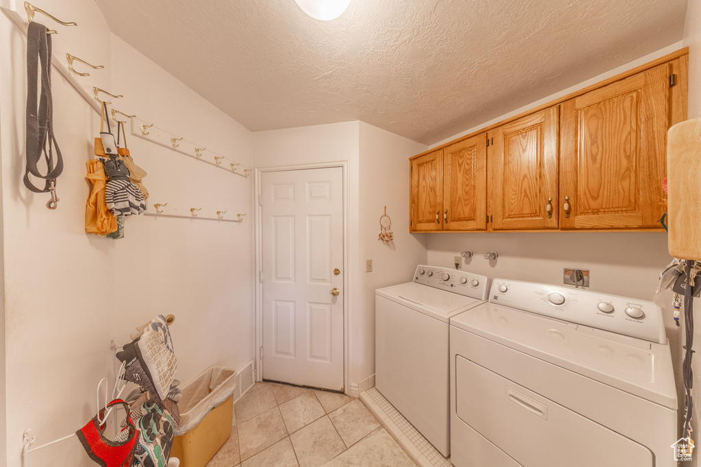 Laundry room featuring cabinet space, washer and dryer, light tile patterned floors, and a textured ceiling
