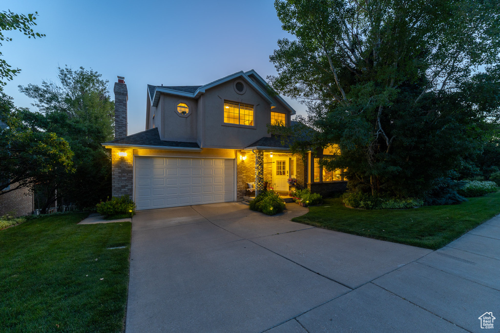 Traditional home featuring a garage, a chimney, driveway, and a front lawn