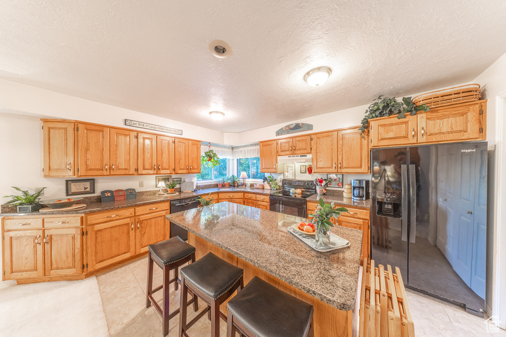 Kitchen featuring black appliances, a breakfast bar, a center island, dark stone counters, and a textured ceiling