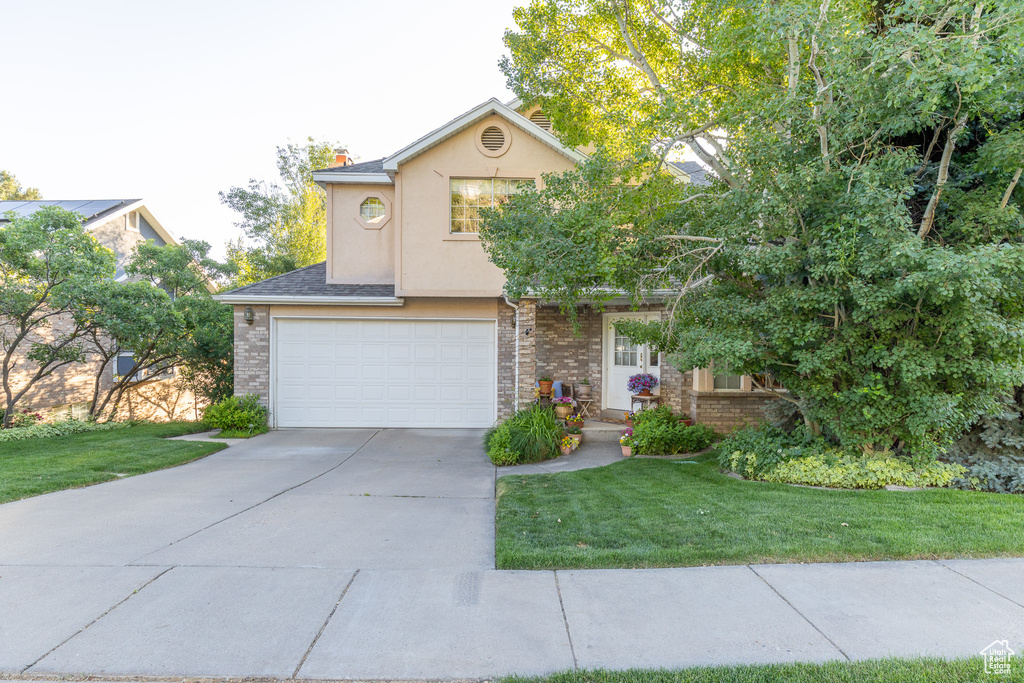 View of front of home featuring a garage, concrete driveway, a front yard, and stucco siding