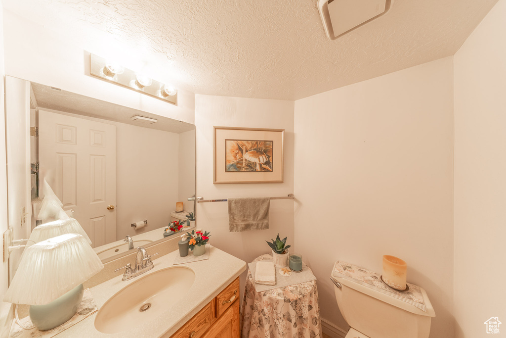Half bathroom featuring toilet, vanity, and a textured ceiling