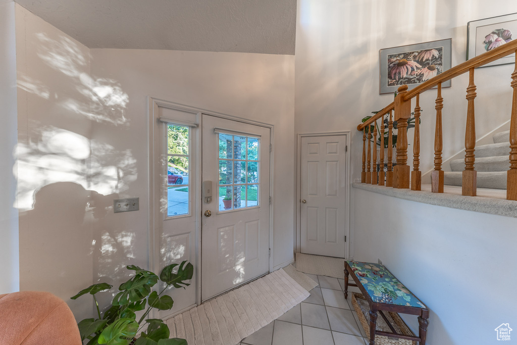 Entrance foyer with stairs, light tile patterned flooring, and vaulted ceiling