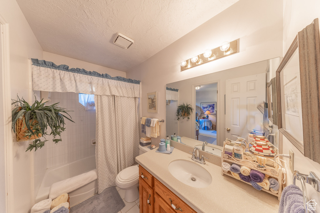 Full bath featuring shower / bath combo, a textured ceiling, tile patterned floors, vanity, and toilet